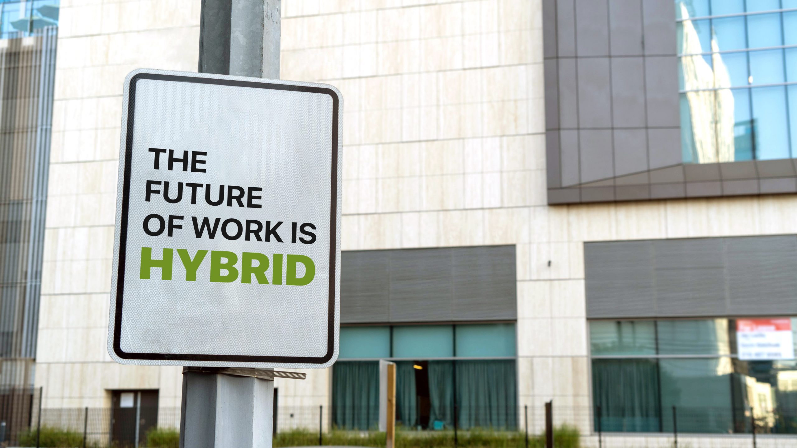 Sign saying the future of work is hybrid with a corporate building in the background
