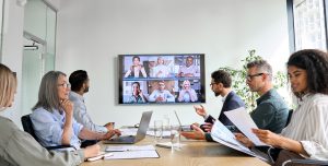 Diverse employees on online conference video call on tv screen in meeting room.